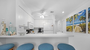 A modern kitchen with white cabinets, a central island with stools, and a ceiling fan.