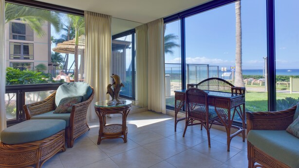 Un balcone con mobili in vimini, un tavolo in vetro e vista sull'oceano e palme.