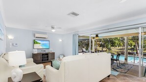 Ein modernes Wohnzimmer mit einem weißen Sofa, einem Fernseher und Blick auf einen Pool.