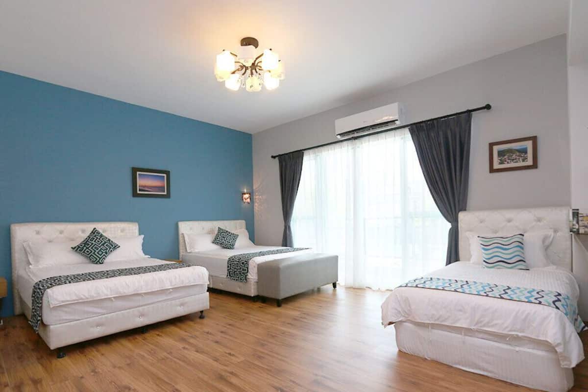 A hotel room with two beds, a sofa, a chandelier, and a large window with curtains.