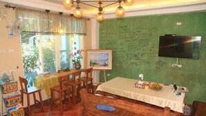 Un coin repas avec une table dressée pour deux personnes, un téléviseur fixé au mur et un tableau noir vert sur lequel on a écrit.