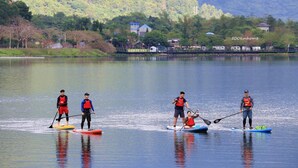 Un groupe de personnes pratique le paddle sur un lac calme, avec une colline boisée en arrière-plan.