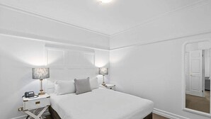 A white-themed bedroom with a large bed, two bedside tables with lamps, and a mirror on the wall. - S&P Apartments - Central Station (Brisbane)