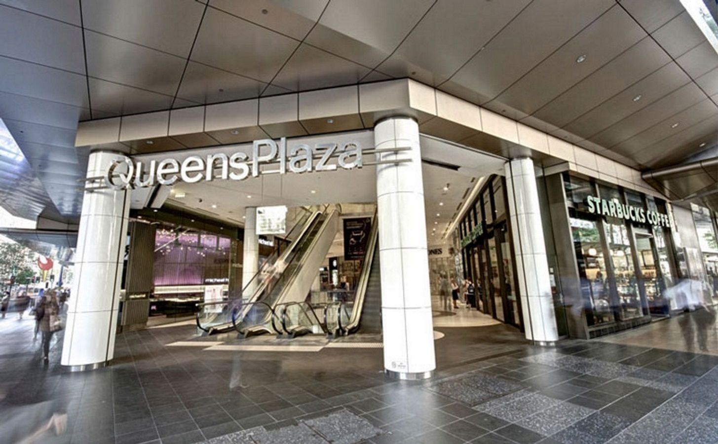 La place Queens, avec un escalier mécanique et un café Starbucks.