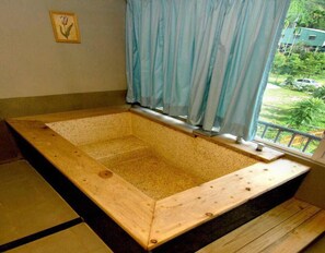Eine hölzerne Badewanne mit Blick auf eine grüne Landschaft durch ein Fenster.