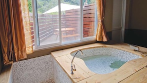 A bathroom with a wooden bathtub, a window with curtains, and a view of an outdoor deck. - CDR Hotspring Resort (Kaohsiung)