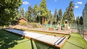 A pool table with a surrounding green artificial turf area, a wooden bench, and a playground with climbing structures and a slide. - Fantastic Forest Setting Rocky Ridge #120 (Tahoe City)