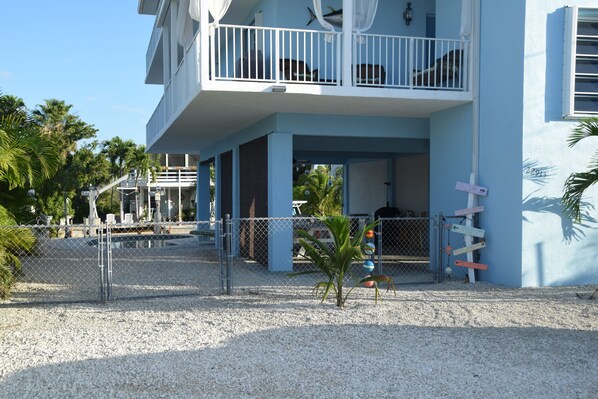 A two-story building with a balcony, a fenced area with palm trees, and a signboard. - Beautiful, 2100 sq ft 3/2 w/ocean views & easy ocean & gulf access. (Cudjoe Key)