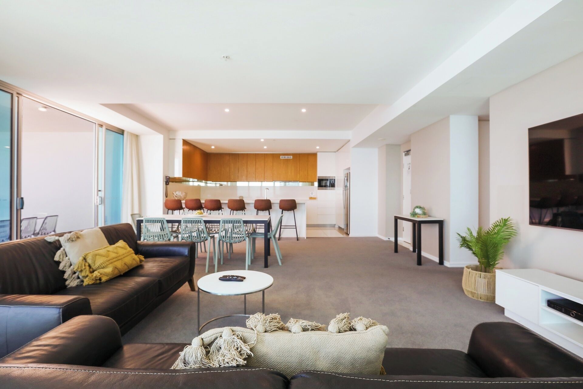 A modern living room with a sofa, coffee table, and a fireplace. In the background, there is a dining area with a table and chairs.