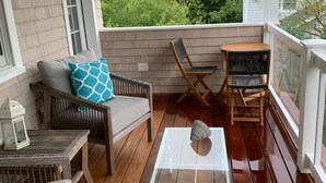 Un terrazzo in legno con tavolo in vetro, mobili in vimini e vista sugli alberi.