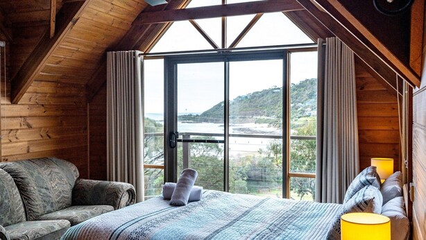 Un dormitorio con un ventanal grande, una cama, un sillón y una lámpara.