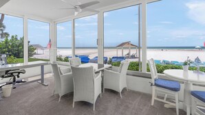 A sunlit room with large windows overlooking a beach, wicker furniture, and a ceiling fan. - Island House Beach Resort 1S (Siesta key)
