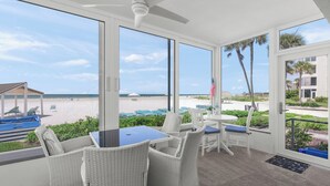 A room with a table and chairs, large windows with a view of the beach and palm trees, and a ceiling fan. - Island House Beach Resort 1S (Siesta key)