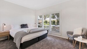 Ein modernes Schlafzimmer mit Bett, Nachttisch, Lampe, Stuhl und Blick durch große Fenster.