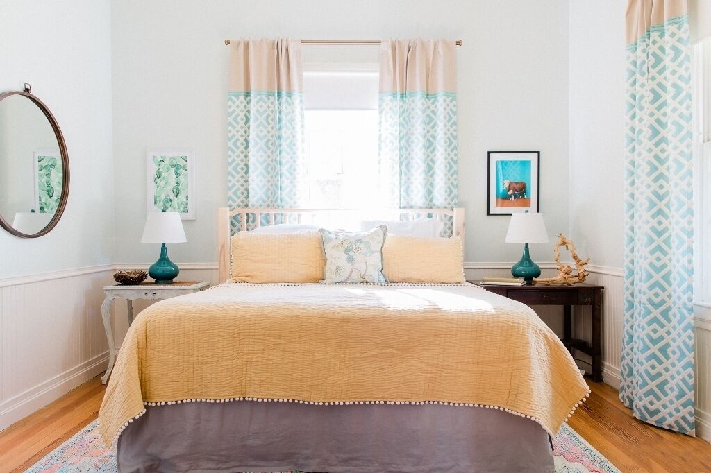 Une chambre à coucher avec un lit, deux tables de chevet, un miroir et des rideaux.