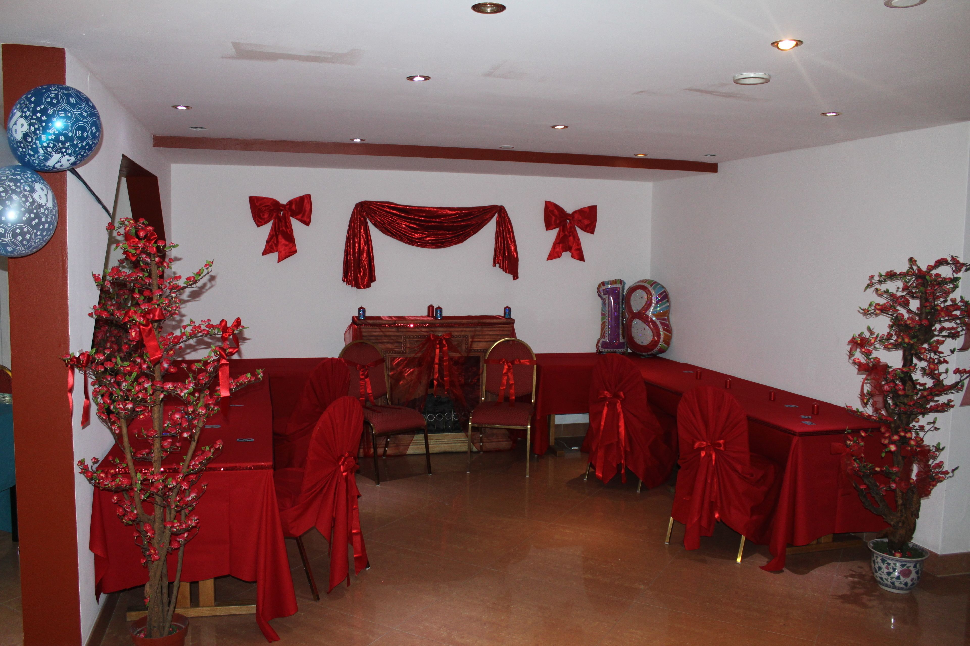 Une pièce avec des fauteuils et des tables recouverts d’un tissu rouge, une cheminée et un sapin de Noël décoré de rouge.