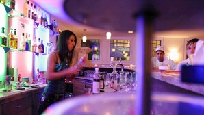 A bar area with a bartender preparing drinks, shelves with bottles, and a counter with glasses and a cash register. - Hotel Langenthal (Langenthal)
