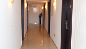 A hotel hallway with doors on both sides, light fixtures on the walls, and a tiled floor. - Hotel Langenthal (Langenthal)