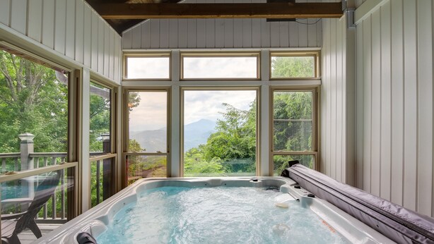 Ein Whirlpool mit Blick auf eine gebirgige Landschaft durch große Fenster.