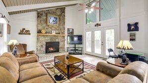 Ein geräumiges Wohnzimmer mit Ledersofas, einem Steincheminée, einem Fernseher und einem Deckenventilator.
