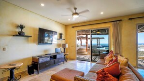 A spacious living area with a large sofa, a television, and a balcony with a view of the ocean. - BEACHFRONT, PRIVATE POOL, GOLF, Concierge, Daily Maid and Chef-Meal Services at Paraiso del Mar (La Paz)