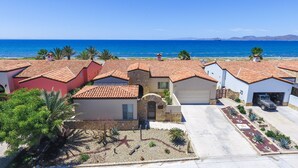 Un quartier résidentiel en bord de mer, avec des maisons aux toits recouverts de tuiles rouges, un ciel d’un bleu éclatant et une vue sur l’océan.