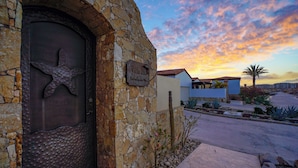 A stone building with a starfish design on the door, a sign reading "Villa 283 - Estrella de Mar," and a view of the sunset. - BEACHFRONT, PRIVATE POOL, GOLF, Concierge, Daily Maid and Chef-Meal Services at Paraiso del Mar (La Paz)
