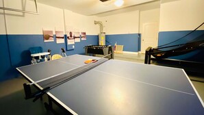 A ping pong table in a room with blue walls, a ceiling-mounted projector, and a door. - 6BR Solterra Pool Home | Spa, Game Room, BBQ, Themed Rooms & 3 Kings (Davenport)