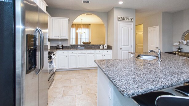 A modern kitchen with white cabinets, a granite countertop, a stainless steel refrigerator, and a pantry sign. - 6BR Solterra Pool Home | Spa, Game Room, BBQ, Themed Rooms & 3 Kings (Davenport)