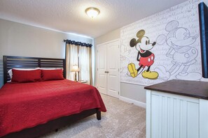 Ein Schlafzimmer mit roter Bettdecke, einer Wandmalerei mit Mickey Mouse, einer weißen Tür und einem Nachttisch.