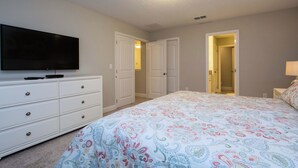 A bedroom with a bed, a dresser, a television, and two doors leading to other rooms. - 6BR Solterra Pool Home | Spa, Game Room, BBQ, Themed Rooms & 3 Kings (Davenport)