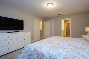 Quarto com cama, cómoda, televisão e duas portas que dão para outros espaços.