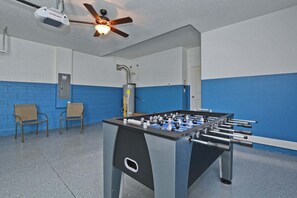 A room with a foosball table, a ceiling fan, and two chairs.