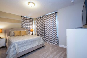 A bedroom with a bed, nightstands, lamps, curtains, and a television.