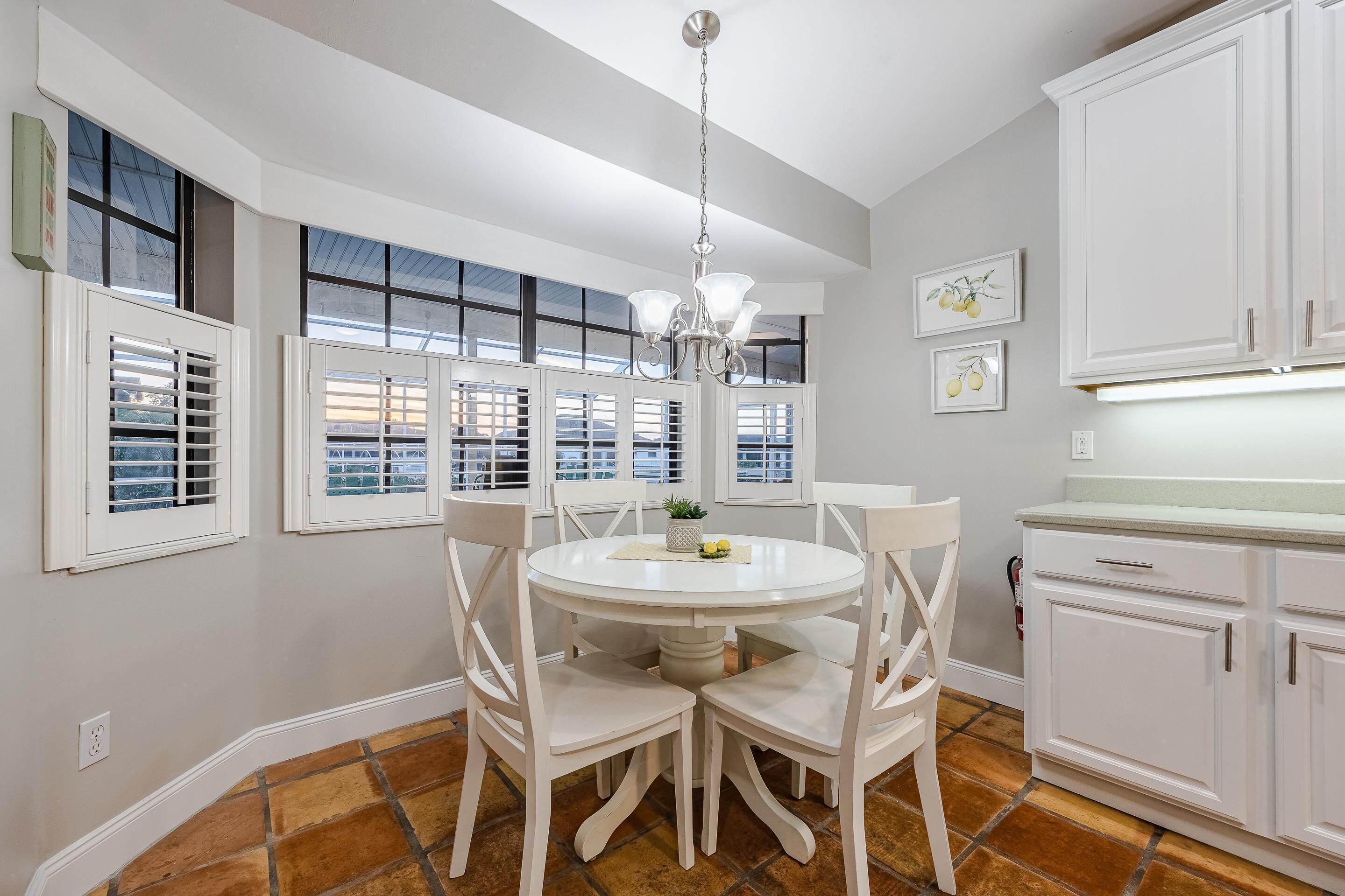 A dining area with a round table, four chairs, a chandelier, and white cabinets.