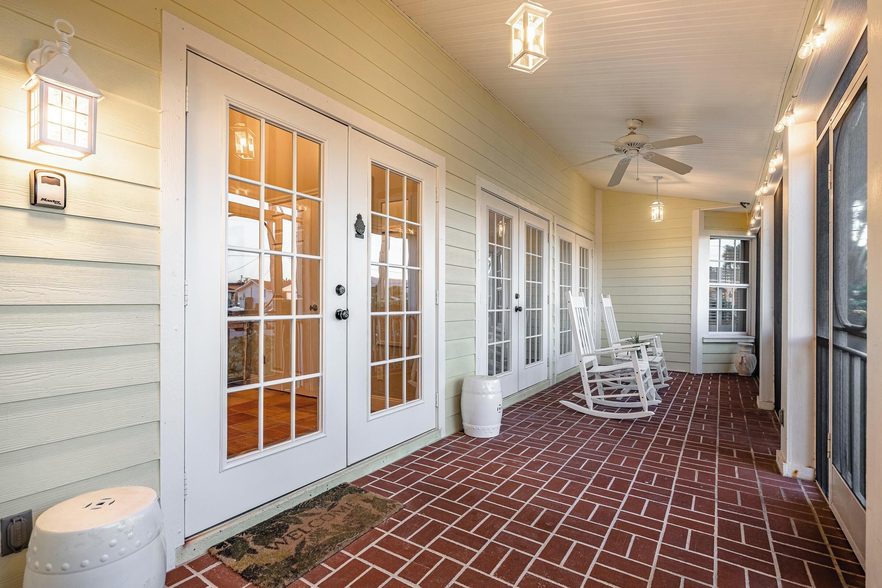 A covered porch with white doors and windows, a ceiling fan, and rocking chairs.