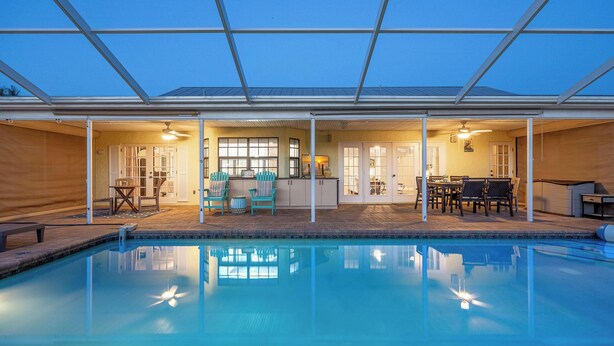En swimmingpool med ett täckt uteområde, ett matbord och stolar.