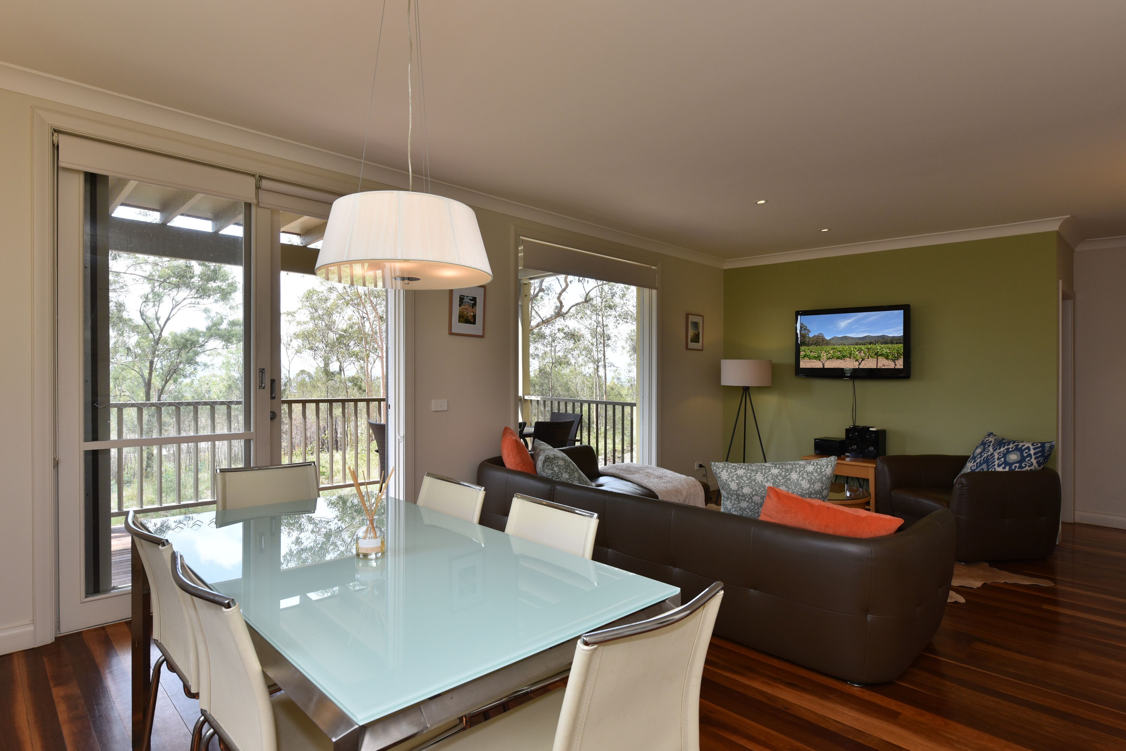 A spacious living area with a glass dining table, a sofa, and a television mounted on the wall.