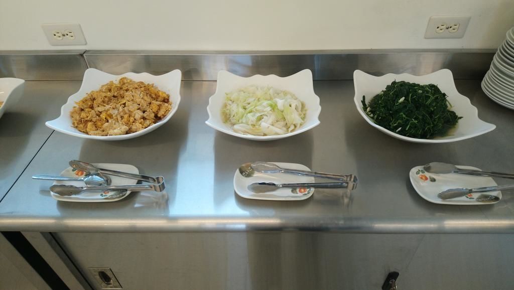 Three white plates with food items on a stainless steel counter.