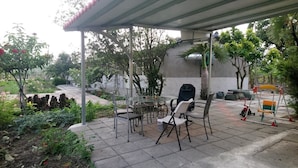 Ein Außenbereich mit einer überdachten Sitzgruppe, einem Grill und einem Spielplatz mit Schaukel und Dreirad.