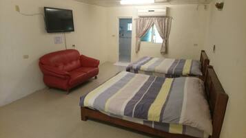 A room with two beds, a red chair, a television, and a shower area.