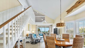 A spacious living area with a dining table surrounded by wicker chairs, a staircase with white railings, and a balcony with a view of the ocean. - Stay and Play all Day in this Very Nice Spacious Beach Resort Villa! C1622A (Englewood)