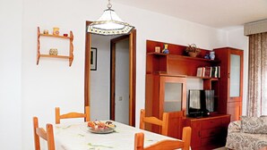 A dining area with a table set for four, a television, and a bookshelf with various items. - Apartment by the beach in Barbate (BARBATE)
