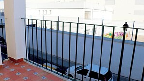 A balcony with a metal railing, a tiled floor, and a view of a street with buildings and a playground. - Apartment by the beach in Barbate (BARBATE)