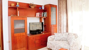 A living room with a wooden entertainment unit, a television, and a patterned sofa. - Apartment by the beach in Barbate (BARBATE)