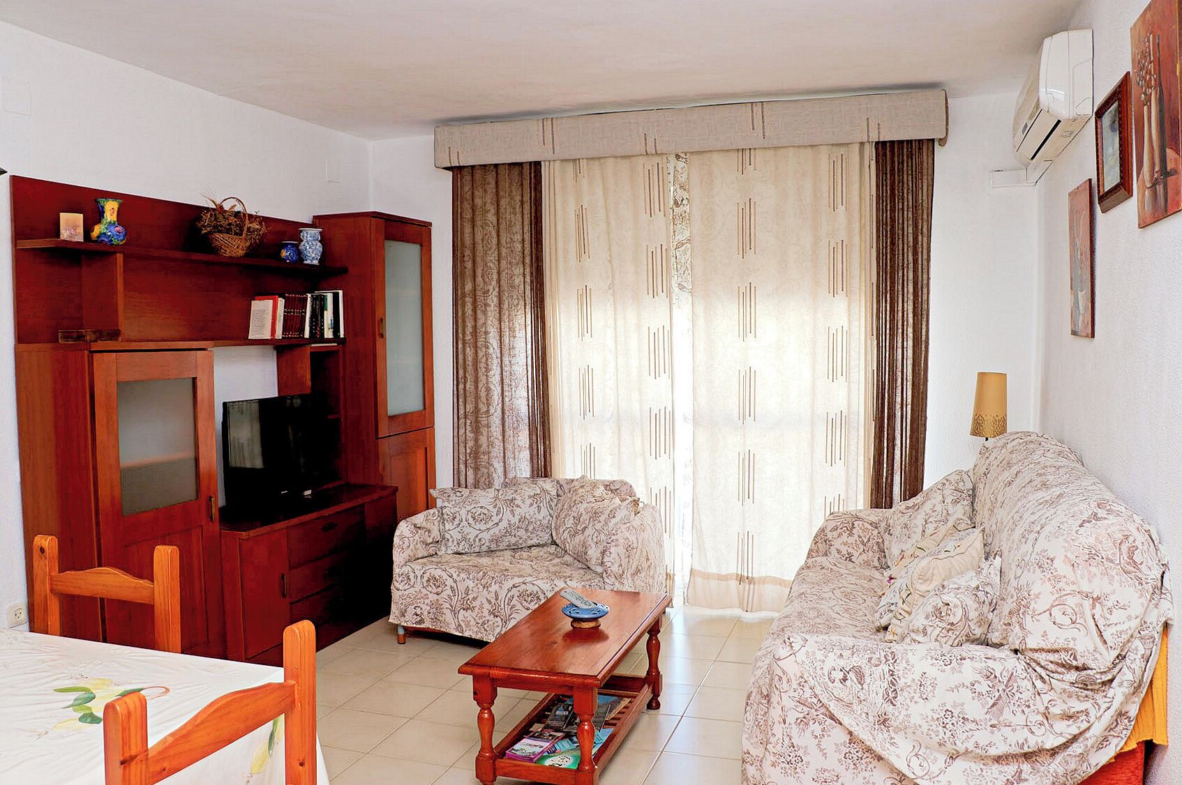 A living room with a television, two patterned sofas, a wooden coffee table, and a bookshelf.