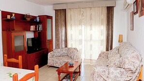 A living room with a television, two patterned sofas, a wooden coffee table, and a bookshelf. - Apartment by the beach in Barbate (BARBATE)