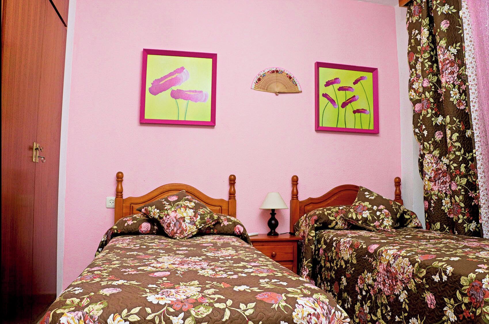A bedroom with two beds, a wooden headboard, a bedside table with a lamp, and two framed pictures on the wall.