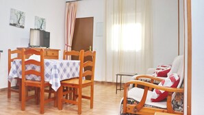 Un coin repas avec une table dressée pour deux personnes, des chaises en bois, un téléviseur posé sur un meuble et un canapé avec des coussins rouges.