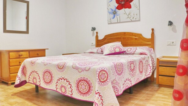 Une chambre à coucher avec un lit en bois, une table de chevet, une commode et un miroir fixé au mur.